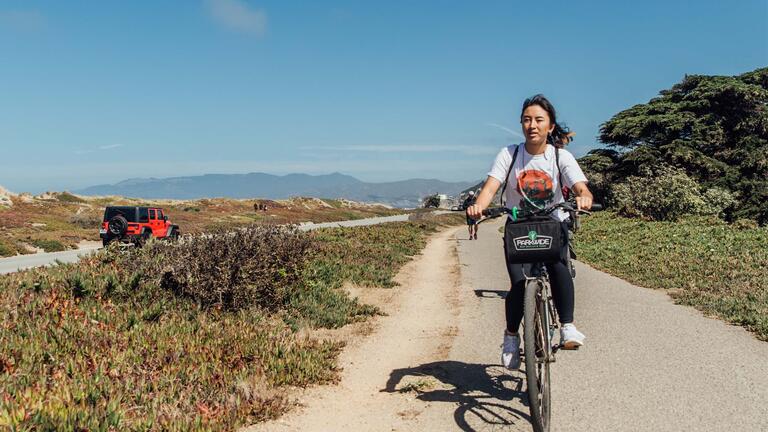 Student rides a bike on a path near the coast.