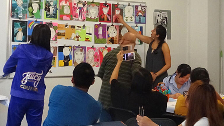 Teacher points to postings on a wall in front of class.