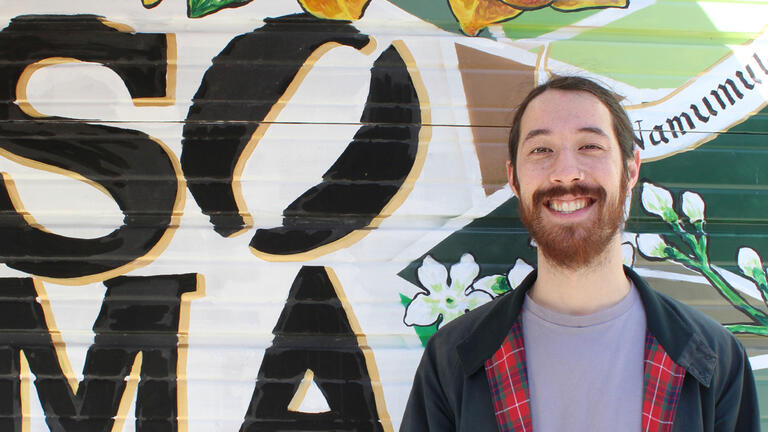 David Woo in front of a mural that reads SOMA