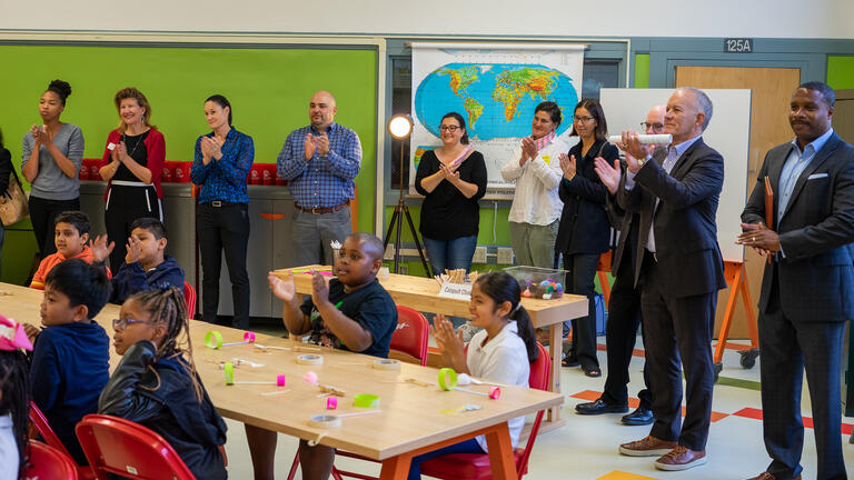 Group of adults stand and applaud while children sit at a table