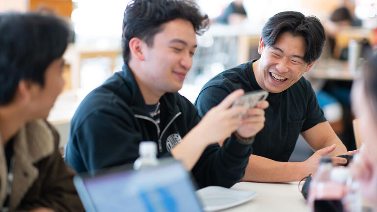 Students chat and laugh at a cafeteria table.