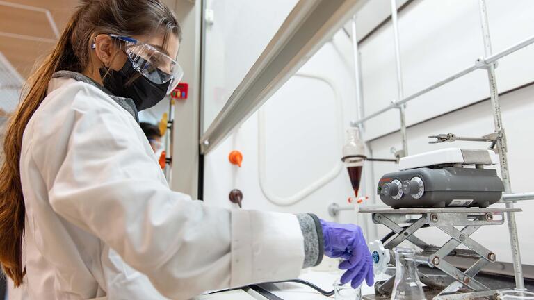 Student wearing protective gear works with beakers in the lab