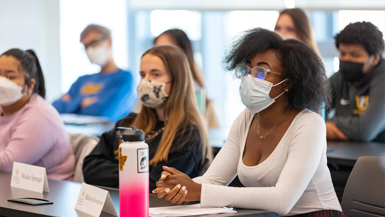 Students with name tags on the table sit in two rows and listen