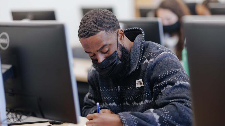 Student sitting in a computer lab writes on a piece of paper