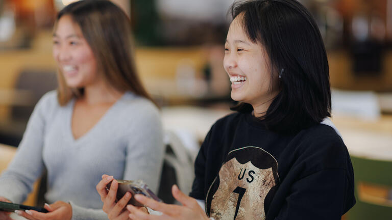 Student smiles in class while holding a phone.