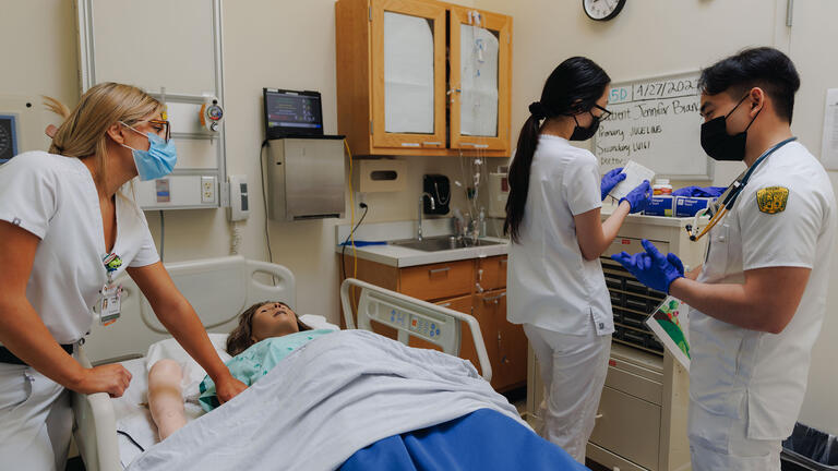 Several students work on a practice dummy in the nursing sim lab.