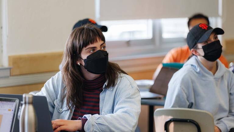 Students with laptops look to the right while listening