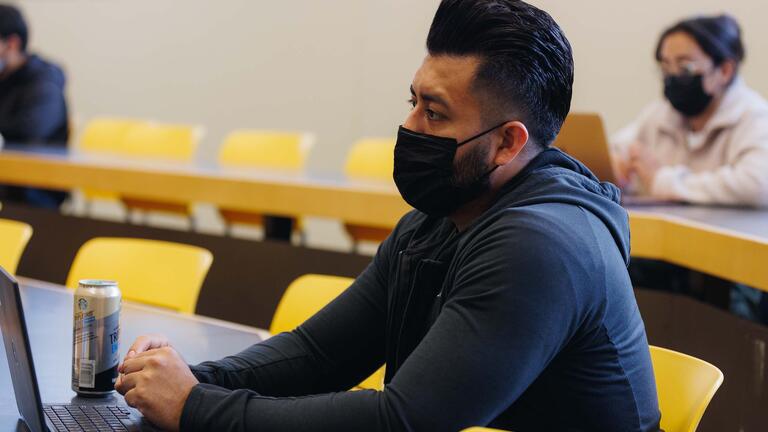 Student with a laptop and a can of drink next to it listens in lecture hall