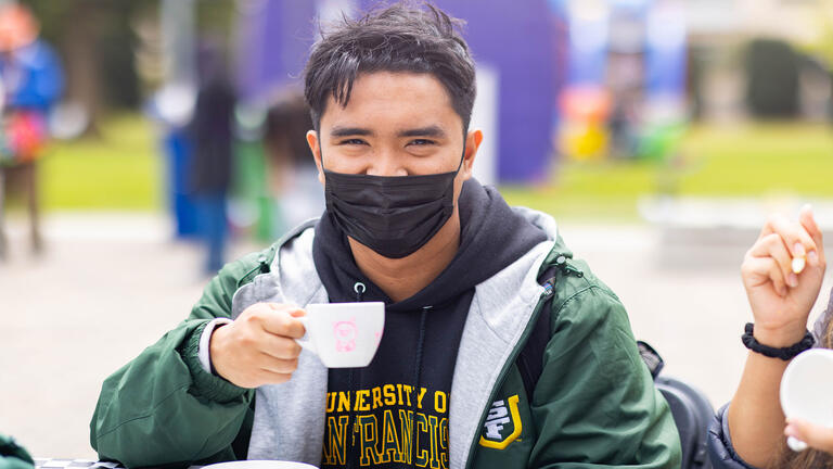 Student sips tea at a table.