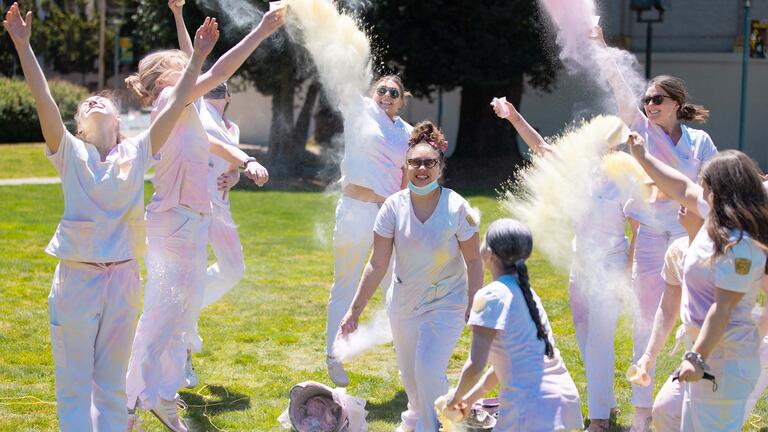 Nursing students throw colored powder in the air at a celebration.