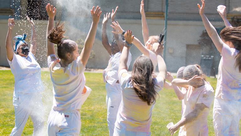 Group of nursing students throw colored powder in the air.