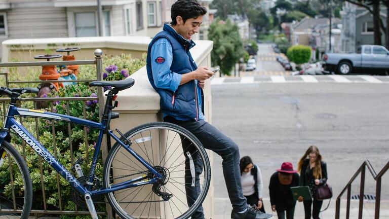Student leans on wall next to bicycle