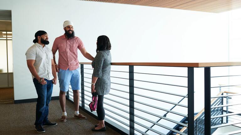 Three students stand and talk near stairs