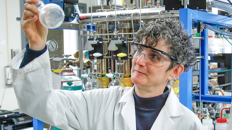 Person in lab coat holding lightbulb.