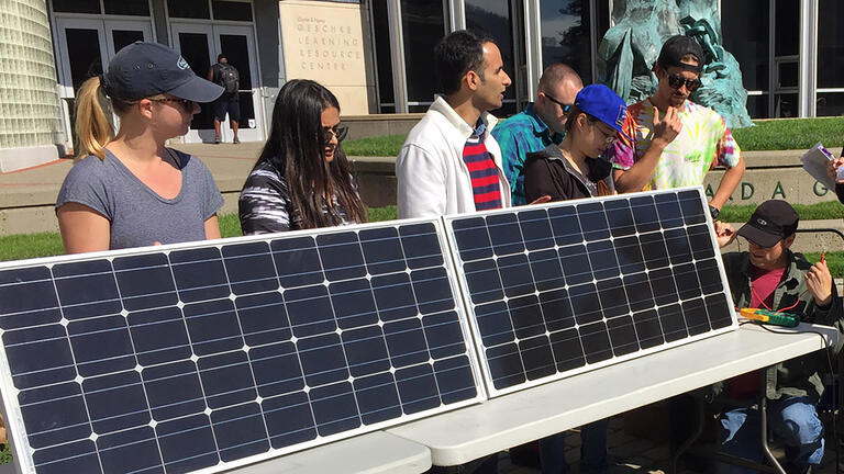 Students standing behind solar panel.