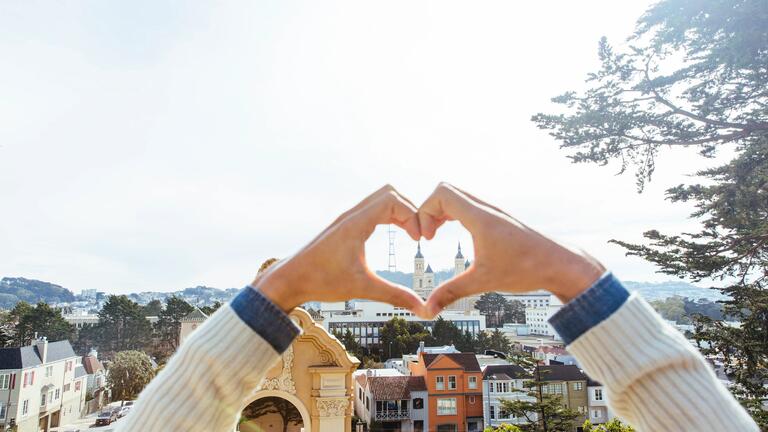Hands forming shape of heart while framing Saint Ignatius church in the distance
