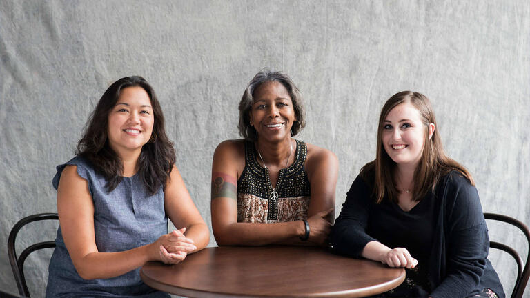 Three students sitting at a table smiling.