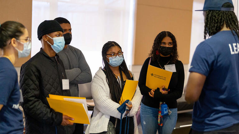 A group of students listen to a staff member at event.