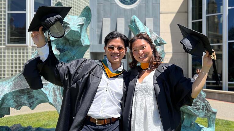 Two graduates wave their hats and pose for picture.