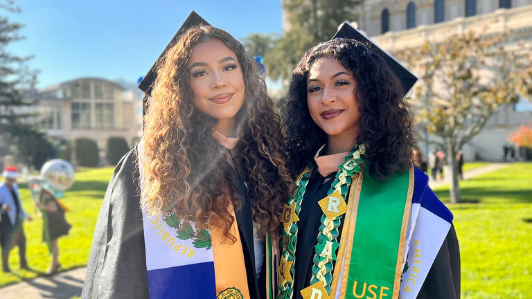 Two graduates in regalia pose on the grass