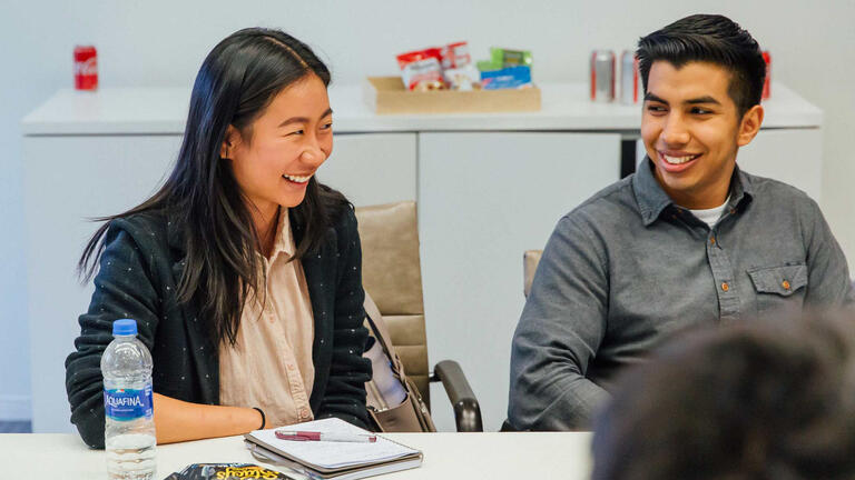 Two students at a table in a classroom laughing.