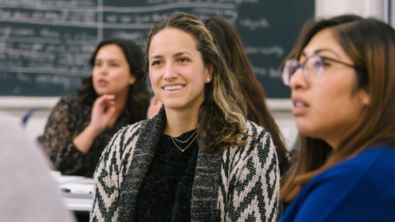 Two students sitting in a classroom having a conversation.