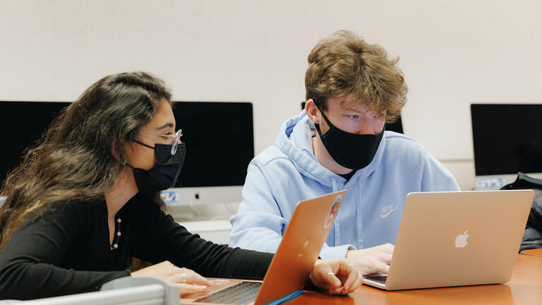 Two students work on laptops in the design computer lab.