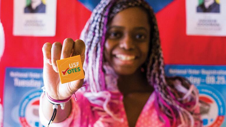 Student smiles and holds a button that says USF Votes.