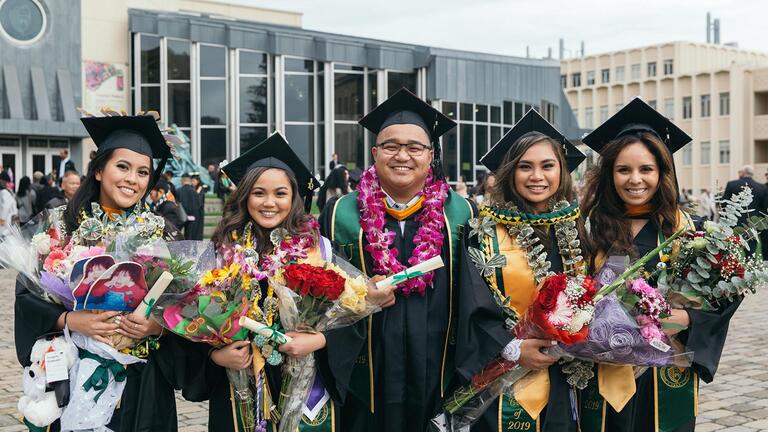 students posing and smiling in their caps and gowns holding flowers 