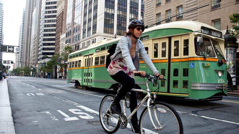 Person biking in Downtown San Francisco with a trolley behind them.