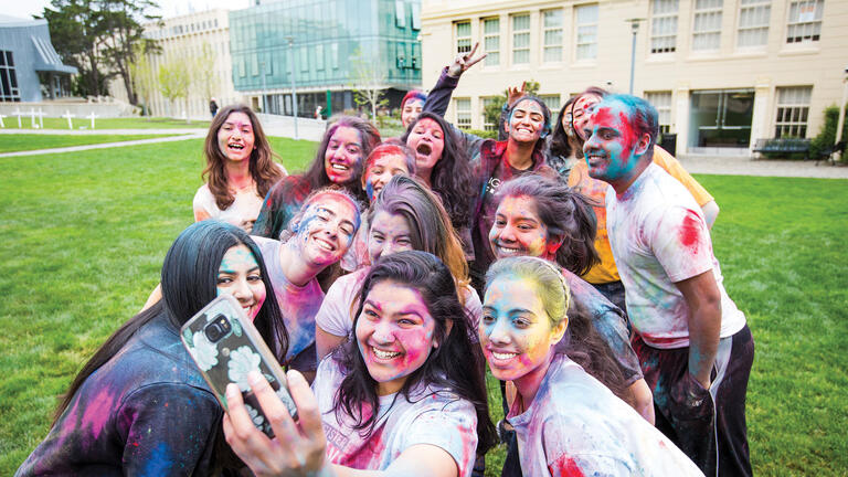 Students covered in colored power pose for a photo on the lawn.