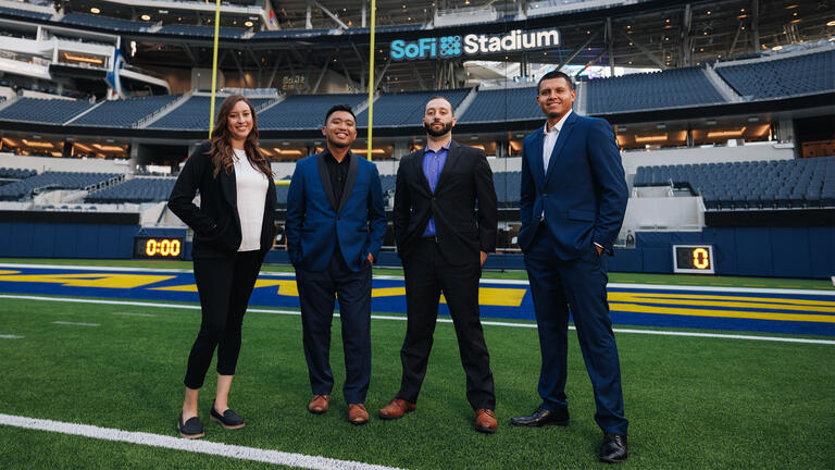 Four Sport Managment students pose on the field at SoFi Stadium.