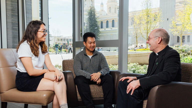 Two students chat with Father Paul Fitzgerald