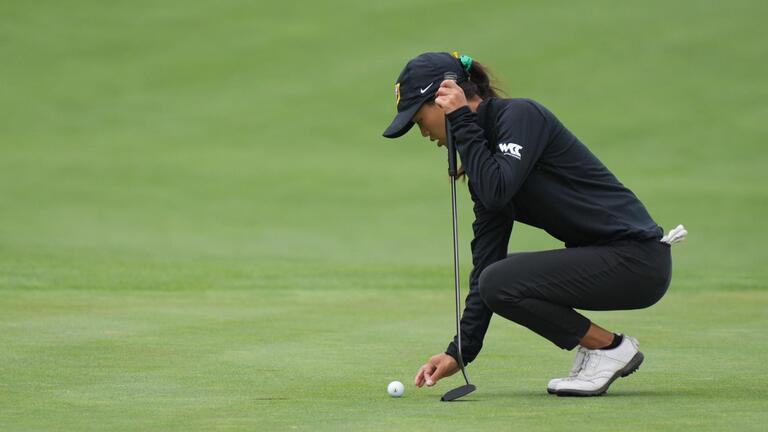 USF women&#039;s golf player kneeling to place golf ball 