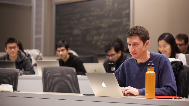 Students in a classroom looking at a laptop