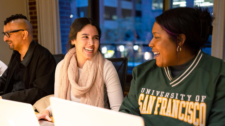 Two USF students chatting while working at their laptops