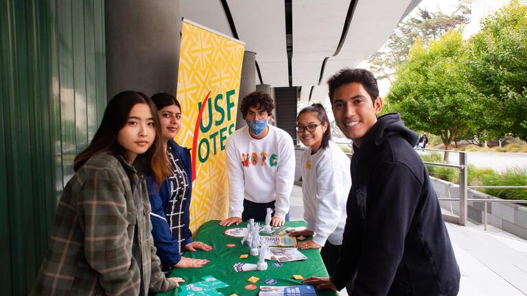 Five USFVotes team members standing around a table