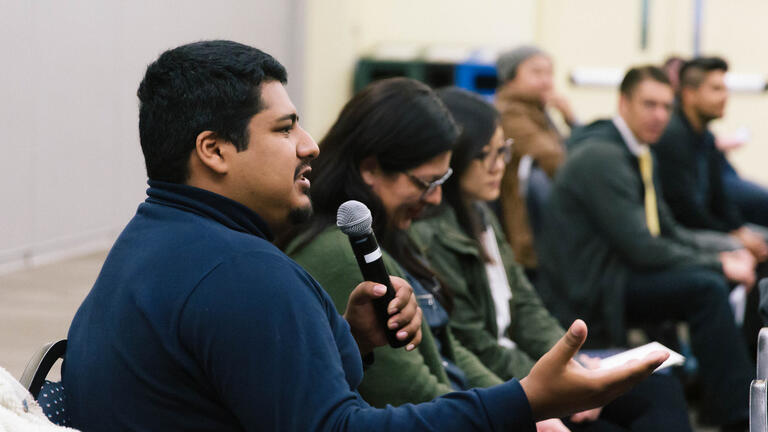 Person speaking into a microphone sitting in a crowd.