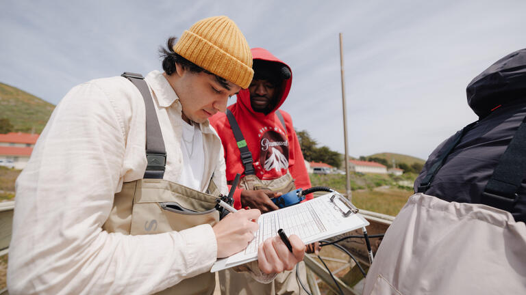 Student writing on a clipboard in a field