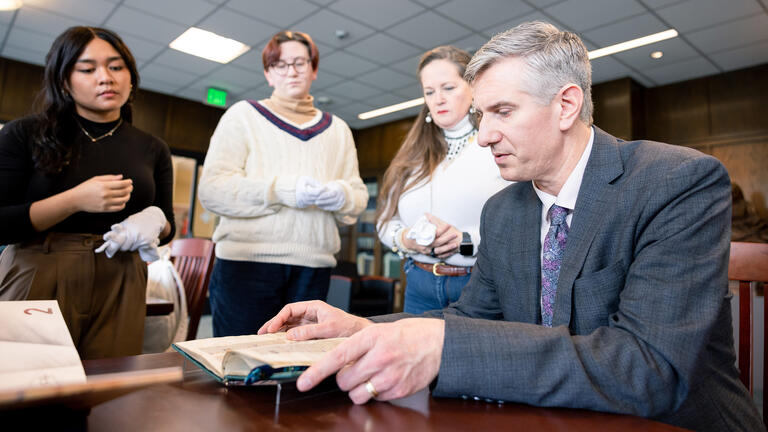 teacher examines book with students looking on