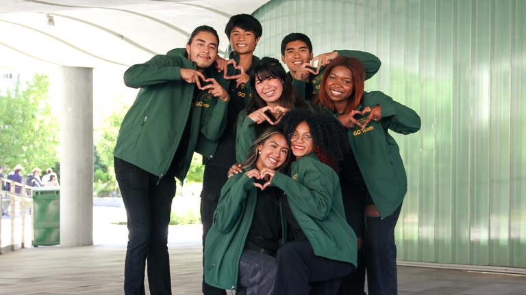 Seven students from GO Team posing with hand heart signals