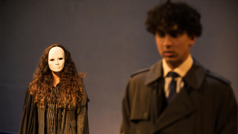 an ominous figure stalks a man during a scene in a play 