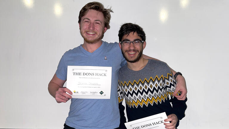 Two students huddle while holding their certificates for hackathon participation.