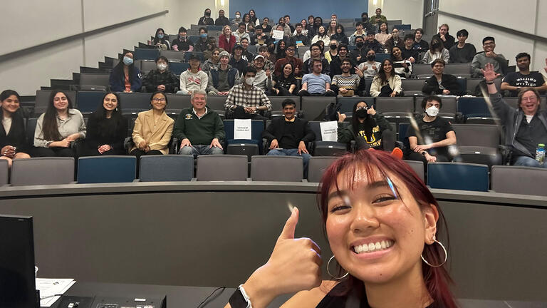 Student takes a selfie with classroom audience behind.