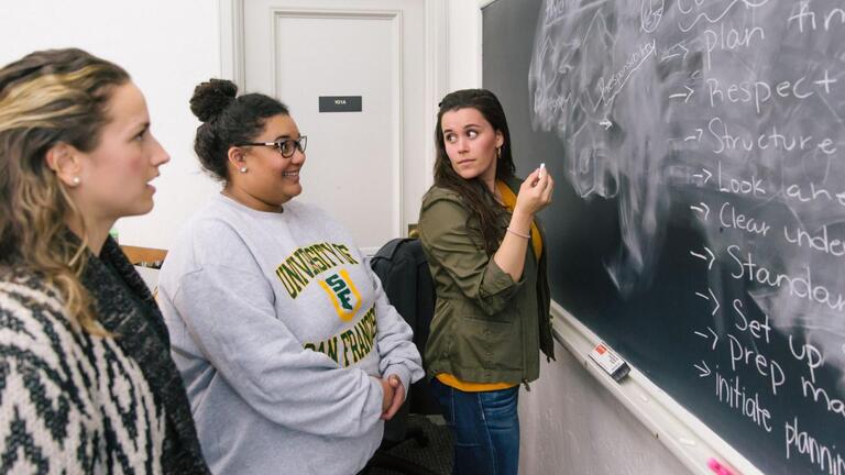 students writing on chalk board
