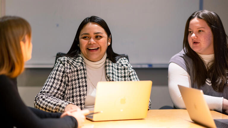 Three students chatting and smiling, working on laptops