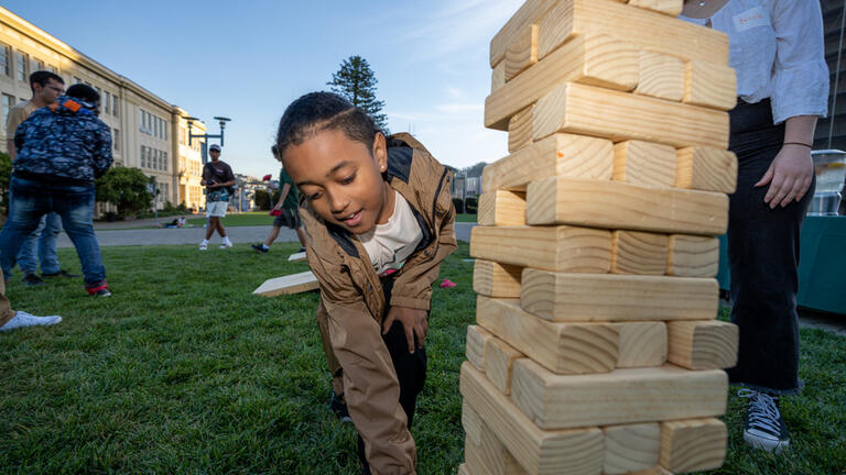 mentee plays giant jenga outside on grass