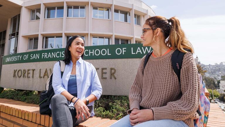 two students sitting by the usf school of law sign