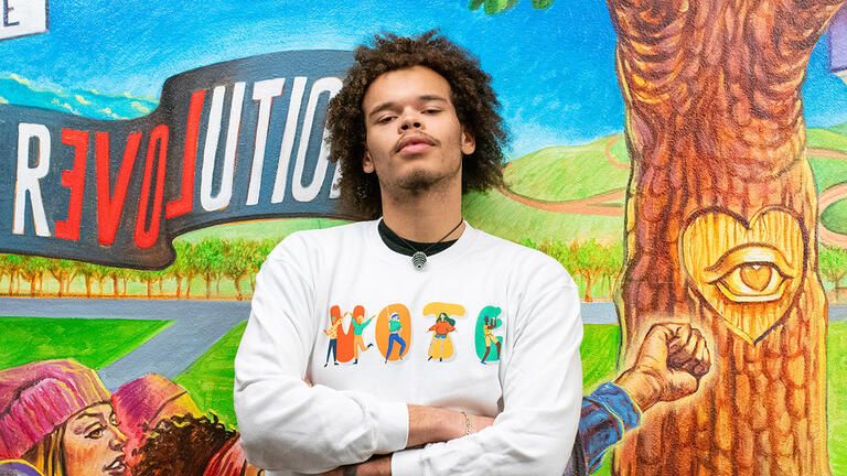 student stands in front of mccarthy center mural