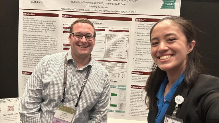Two people taking a picture together in front of a research poster